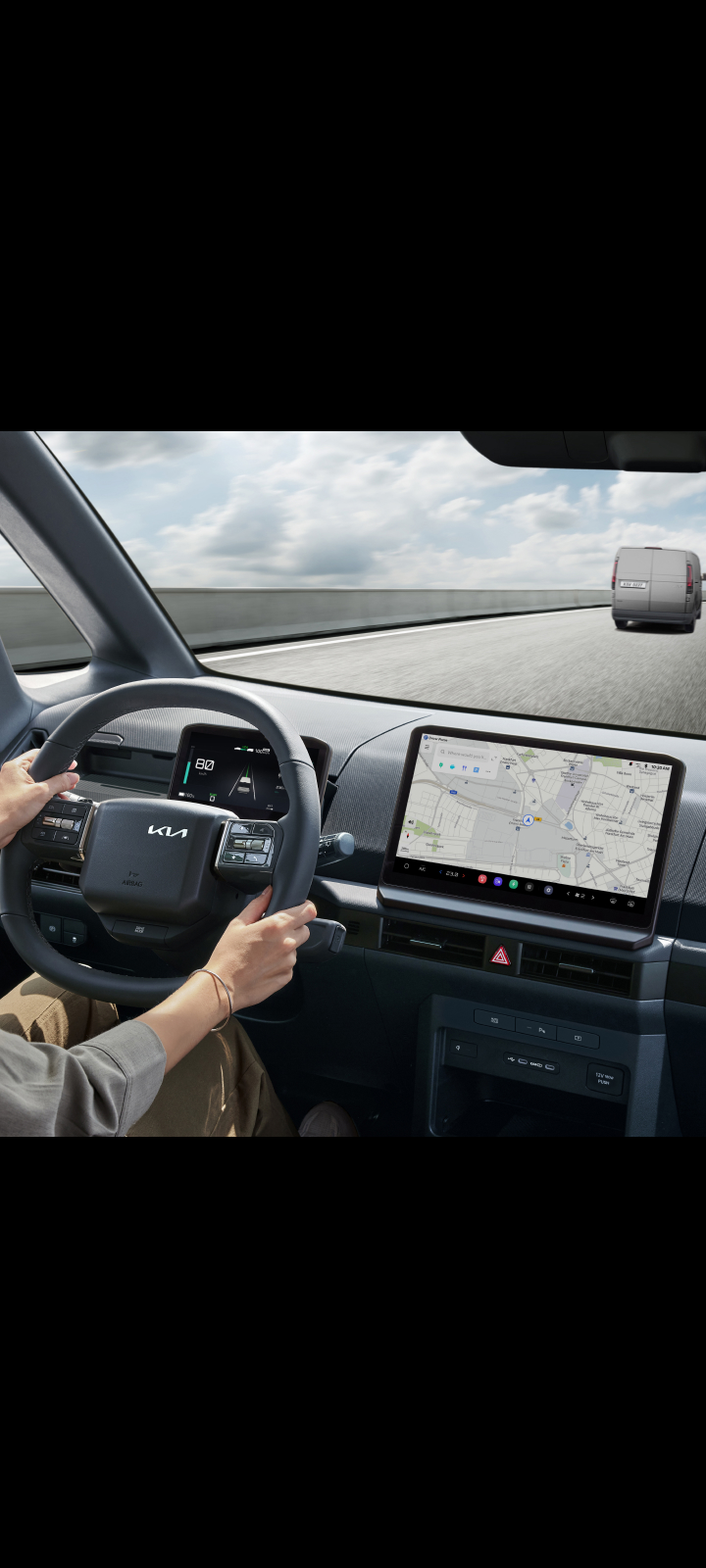 Fahrer hält das Lenkrad des Kia PV5 Cargo. Das Navigations-Display ist gut sichtbar.